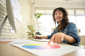 Asian female graphic designer talking on mobile phone with colleague or customer while working in office. Select focus to finger.