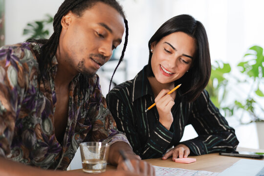 Two diverse young professionals collaborate on a project at a modern office desk. They are reviewing documents and discussing ideas with a positive attitude.