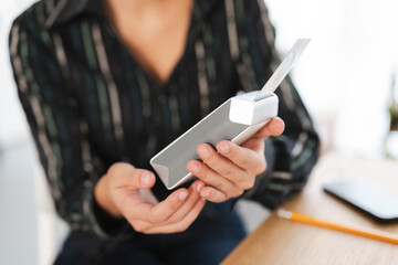 A person in a striped shirt holds a modern grey and white electronic device. They are inserting a white component into the gadget. A light indicator is visible on the device.