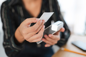 A person holds a payment card near a mobile payment terminal connected to a smartphone. They are completing a secure, contactless transaction. The card shows a green light, indicating connection.