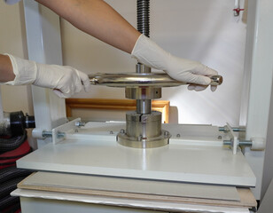 Gloved hands rotate the handle of the screw press. Paper pressing and straightening, bookbinding workshop, close-up.