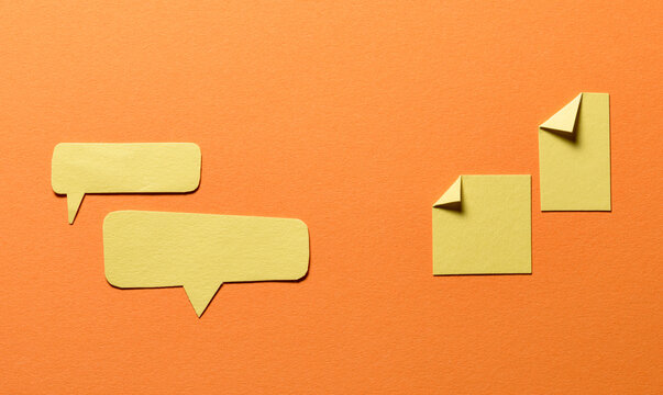 Yellow speech bubbles and paper memo notes with folded dog-ear earmark and copy space for text on orange background, communication dialog concept top view flat lay