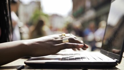 African woman using laptop at outdoor cafe for remote work and communication, typing on keyboard, sunlight, online. - Powered by Adobe