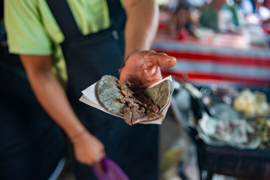 A street vendor displays a freshly made cecina taco with blue corn tortilla