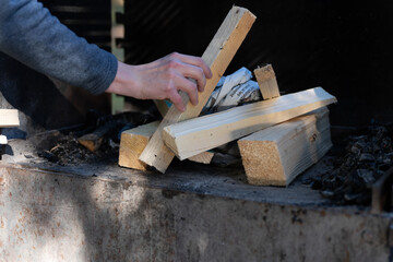 Hand placing firewood in barbecue while preparing for grill