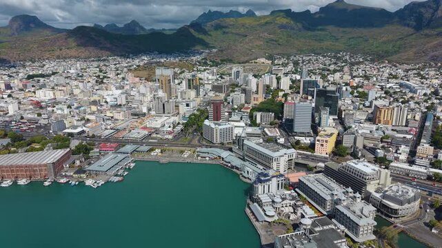 Pull out drone shot of Port Louis skyline in Mauritius. Features the bustling Caudan Waterfront, with the city nestled against the Moka Mountains and the blue ocean.