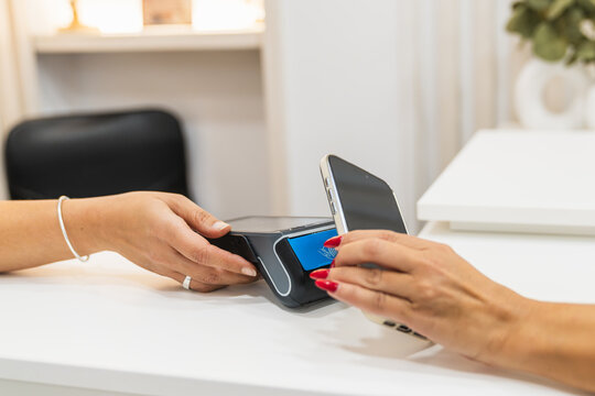 Customer paying with a mobile phone on a payment terminal, completing a transaction in a physiotherapy or beauty clinic - Powered by Adobe