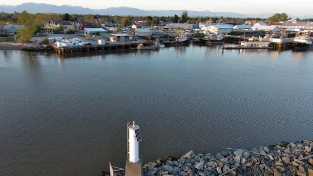 Drone moves around the Becon at the breakwater to marina on a sunny day mountian in background