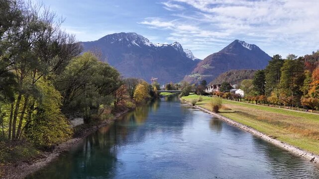 The Linth River near Weesen, Switzerland, flows between tree-lined banks with autumn color, leading toward snow-capped alpine mountains. Nature, travel, and environmental footage for various uses.