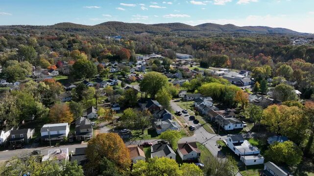 Aerial approaching shot of green residential area in suburbia of USA. Descending shot. Multicolored trees in suburb of American town. Sunlight and blue sky in neighborhood of America.