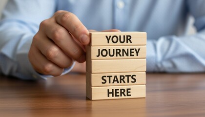 Person's hand stacking wooden blocks with 'Your Journey Starts Here' message on a table, symbolizing new beginnings.