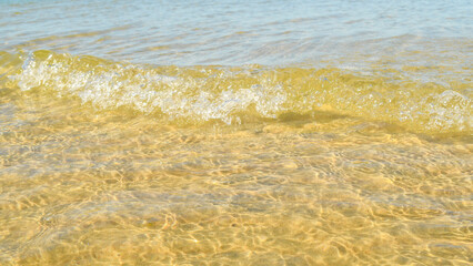 A background of clear water over a sandy bottom. Shallow water with yellow sand. Gentle ripples on the surface. Glittering reflections on the sea.