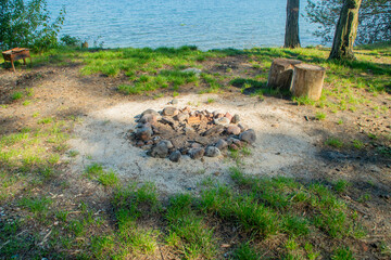 A place with an extinguished campfire on the seashore. A fire pit lined with sea pebbles. A campsite with old bonfire for tourists.