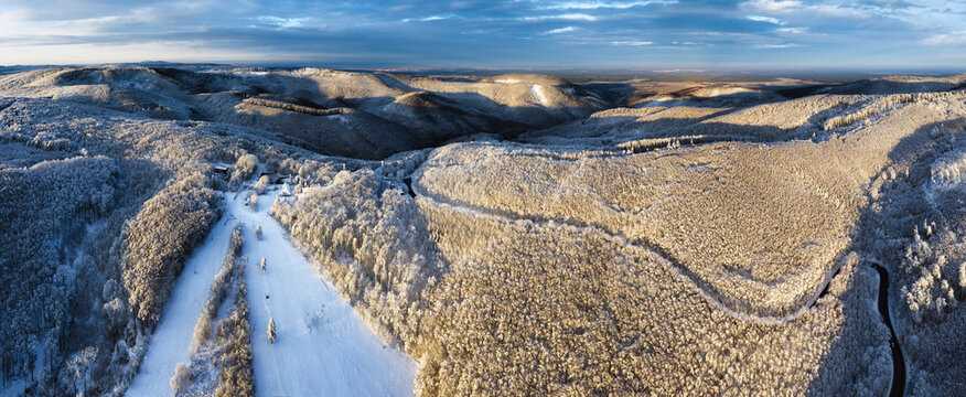 Aerial view of winter forest covered in snow at sunrise with road and ski slope - Powered by Adobe