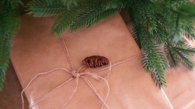 Brown paper gift tied with twine, decorated with pine cone, under green fir tree branches