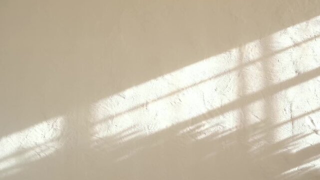 Warm beige textured wall with diagonal sunlight stripes and subtle shadow patterns cast from window blinds.