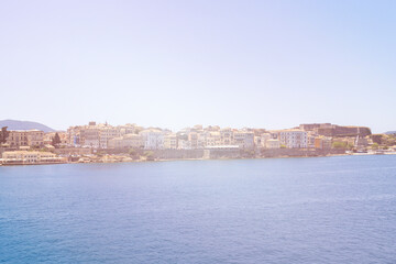 Fototapeta premium Corfu sunlit shoreline and deep blue sea frame docked ships and distant buildings, Greece