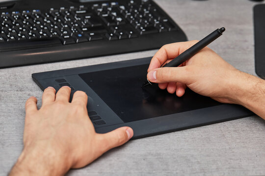 male hands drawing and retouching image on pc computer, using graphic digital tablet and stylus pen at office desk.