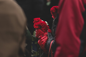 Red carnations in female hands in red leather gloves. Red and black. Red leather gloves. Military widow. Honoring the memory of fallen soldiers. Mourning flowers. Elegant woman. 