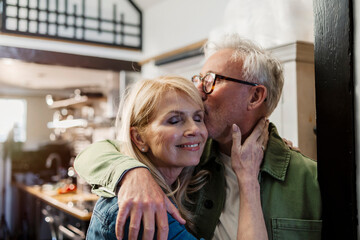 Senior couple embracing in the kitchen with affection and love