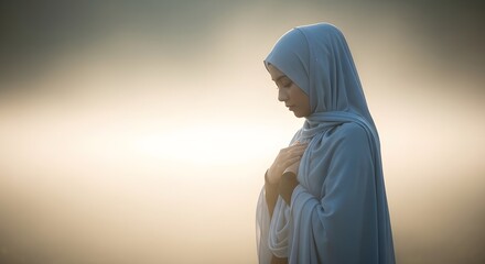 A woman wearing a light blue hijab and modest clothing stands in a peaceful outdoor setting with a soft, blurred background during sunset or sunrise, conveying serenity and contemplation