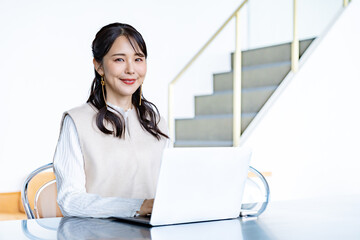 カフェまたは自宅のような明るい空間で、女性がノートパソコンの前に座り仕事をするシーン。