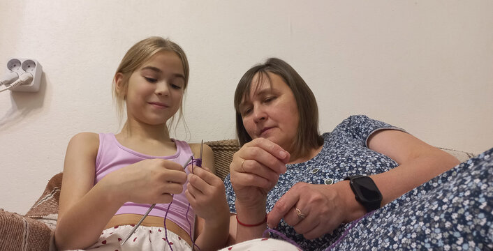 Mother and daughter knit socks in a cozy home kitchen.