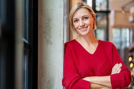 Smiling businesswoman in red sweater at modern office indoors - Powered by Adobe