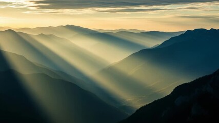 Epic mountain range panorama with golden sunbeams breaking through clouds. A majestic and serene wilderness landscape with layers of misty hills creating a sense of depth