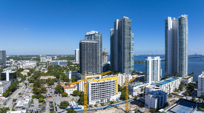 Aerial view of the glittering Edgewater skyline meeting the vast, azure bay under a clear sky, cranes stand tall amidst the modern architecture, Edgewater, Miami, United States.