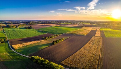 Aerial view of farmland at sunset, showing diverse fields and textures under a vibrant, warm sky