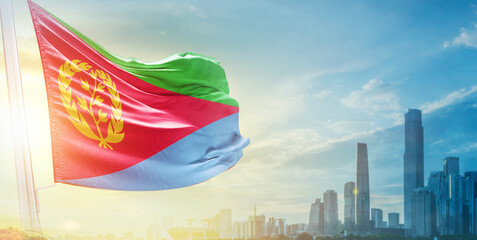 Eritrea flag wavering in beautiful clouds with building skyline. The flag with drone shot in...