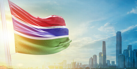 The Gambia flag wavering in beautiful clouds with building skyline. The flag with drone shot in beautiful sky. The Gambia national flag for independence day.