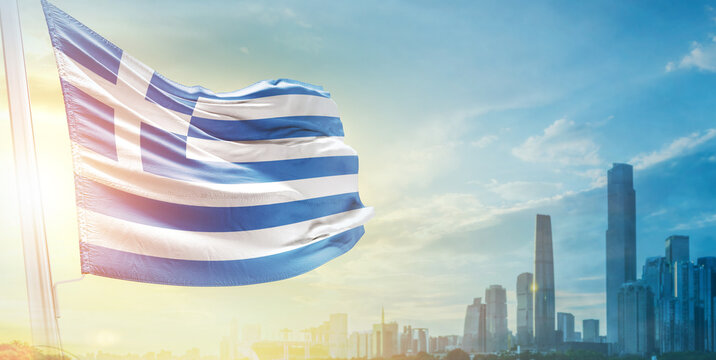 Greece flag wavering in beautiful clouds with building skyline. The flag with drone shot in beautiful sky. Greece national flag for independence day.
