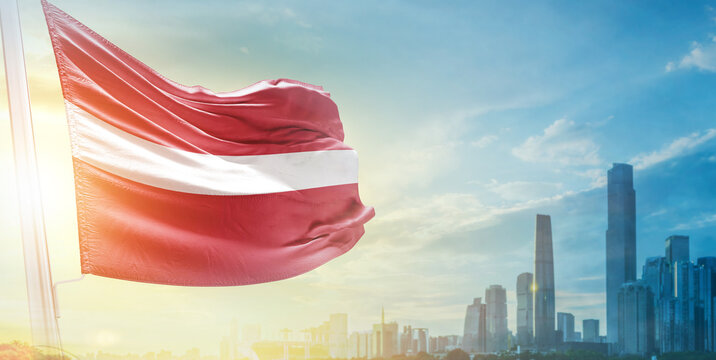 Latvia flag wavering in beautiful clouds with building skyline. The flag with drone shot in beautiful sky. Latvia national flag for independence day. - Powered by Adobe