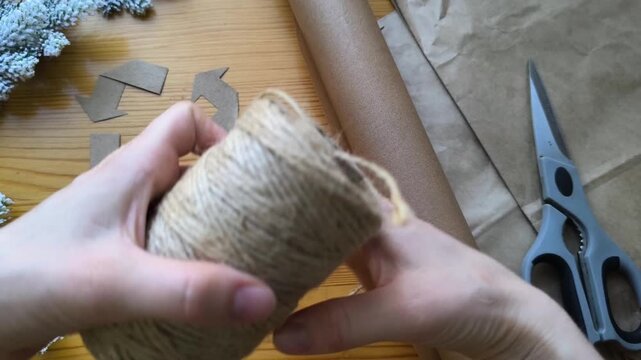 woman's hand removes twine from a skein. Eco-friendly Christmas gift wrapping materials, recycling sign.
