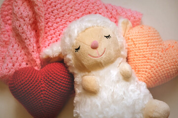 Cute white sheep and crochet colorful hearts, toys and home decoration with soft toys on bedroom for children and nursery. Creative handmade crochet animals background.