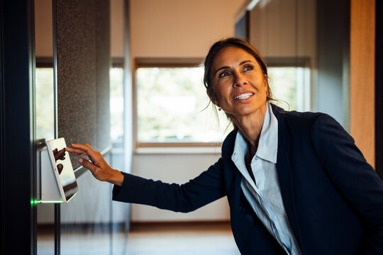 Businesswoman using touchscreen sensor for access in modern office hallway