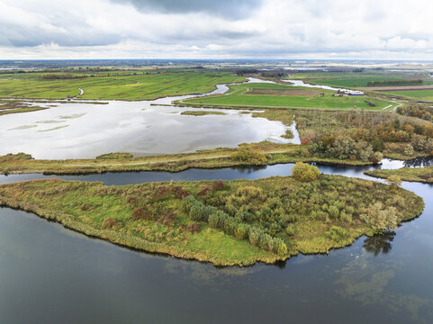 Aerial view of the waterways surrounding a verdant island, where the dark waters contrast against the autumnal foliage, Noordwaard, national park Biesbosch, Noord-Brabant, Netherlands.