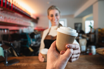 A friendly blonde waitress serves a to go coffee while the cafe owner stands behind the counter supporting smooth business service