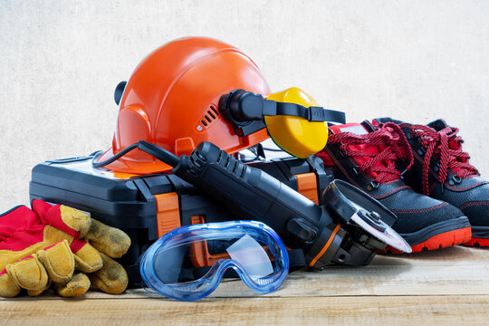 Work personal protective equipment, clothing and angle grinder on wooden desk.