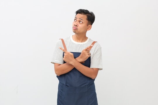 Handsome asian male in apron thinking what do, look sideways thoughtful, cross hands chest pointing left and right, making choice, thinking what pick, taking important decision white background