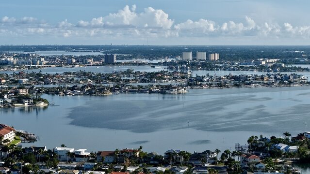 Aerial view of the tranquil waters reflecting the sky, surrounding the buildings and houses of the city under a cloudy sky., St. Pete Beach, Florida, United States.