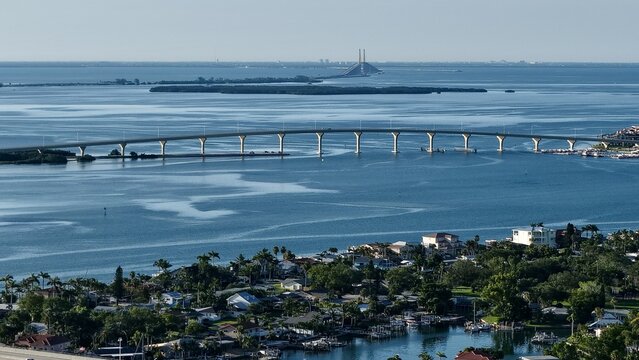 Aerial view of a bridge stretching across sparkling waters towards distant islands and the Sunshine Skyway Bridge, St. Pete Beach, Florida, United States.