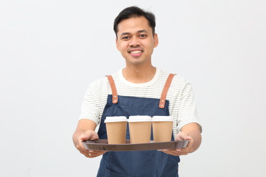 Friendly Asian barista smiling at camera in blue apron carrying tray of takeaway drink orders, standing on white background.
