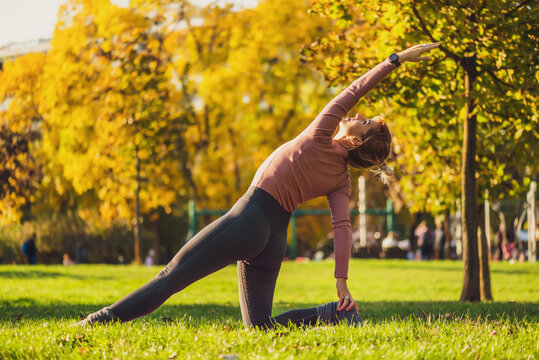 Adult woman practicing pilates in park in autumn. Healthy lifestyle. Side plank exercise.