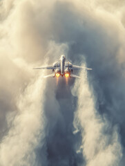 Fighter jet soaring through dense clouds with afterburners blazing, leaving a dramatic trail of vapor trailing behind in dynamic mid-flight action
