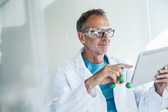 Smiling man in lab coat using tablet PC with molecular structure near wall