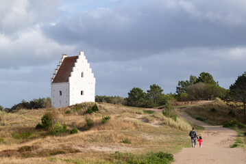 Father holding hand his daugther and walking arround  Den Tilsandede Kirke located in Skage, Denmark.