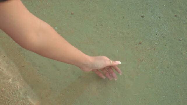 Hand touching water on sandy beach, serene moment, calming vibe